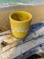 The Lil Brew handcrafted yellow ceramic tumbler with a creamy white drip glaze rim sitting on a weathered wooden plank.