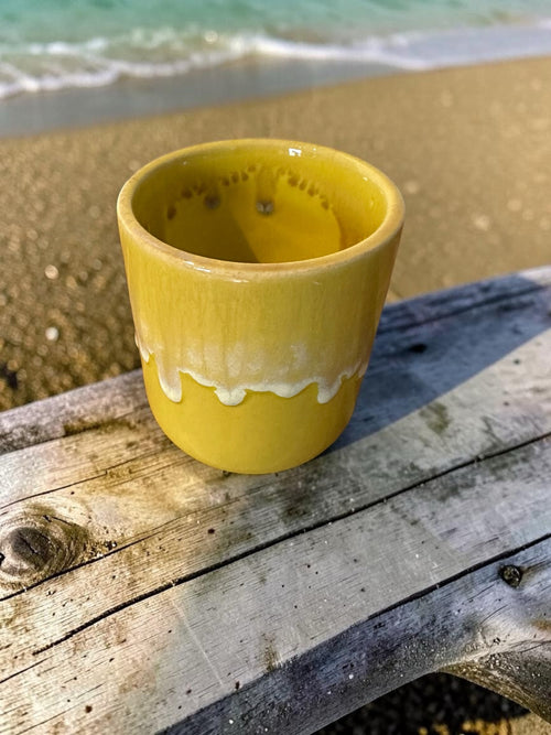 The Lil Brew handcrafted yellow ceramic tumbler with a creamy white drip glaze rim sitting on a weathered wooden plank.